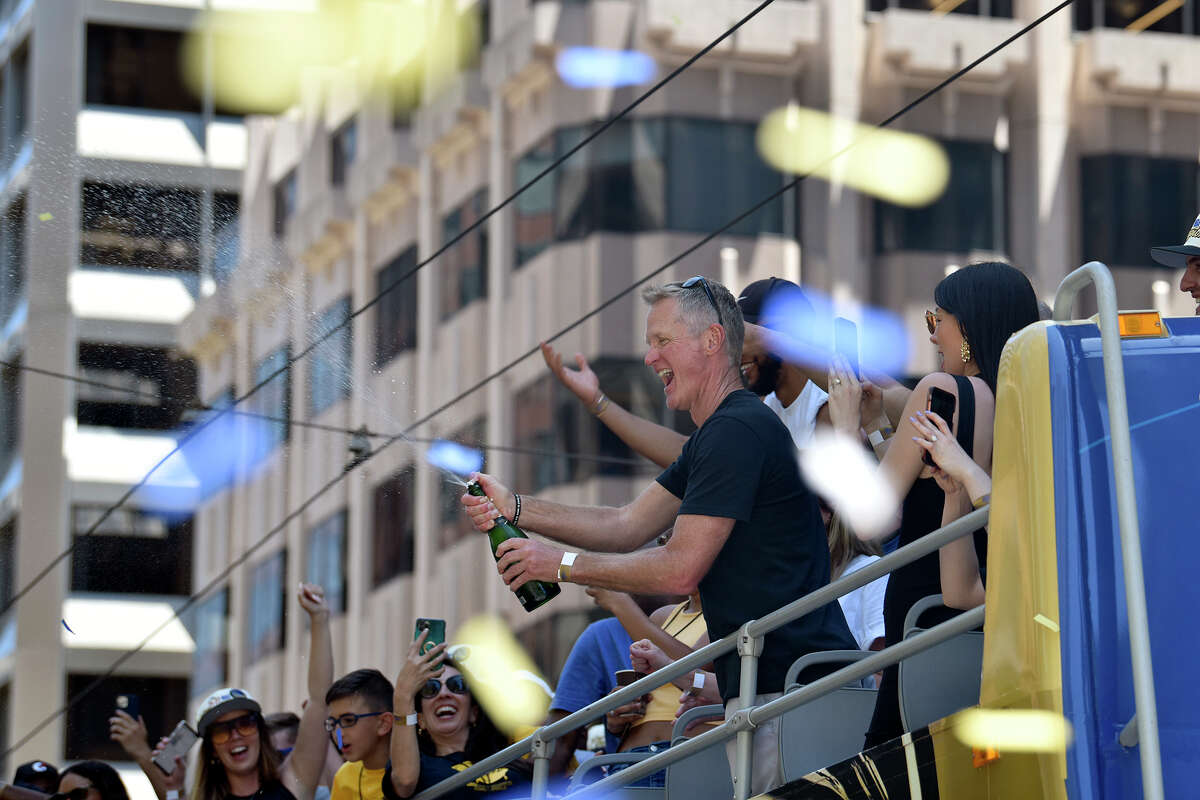 Warriors coach Steve Kerr opens a bottle of champagne from the top of his bus during the team's victory parade on Market Street, Monday, June 20, 2022. 