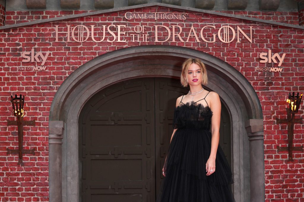 Millie Alcock in a black dress against a brick wall. 