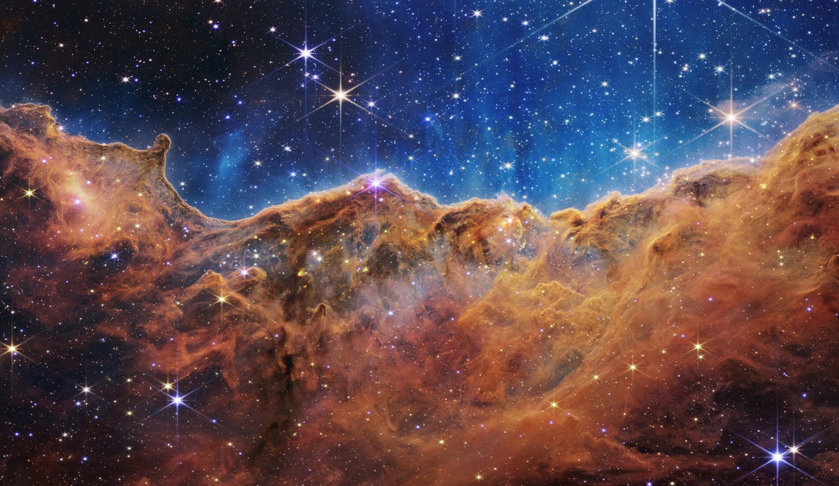 The Carina Nebula: Stars sparkle against an indigo background above rusty bronze gas clouds