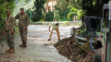 National Guard forces direct traffic as Resident Luis Nogueira helps clear a road damaged by Hurricane Fiona in Cayai, Puerto Rico, on Tuesday.