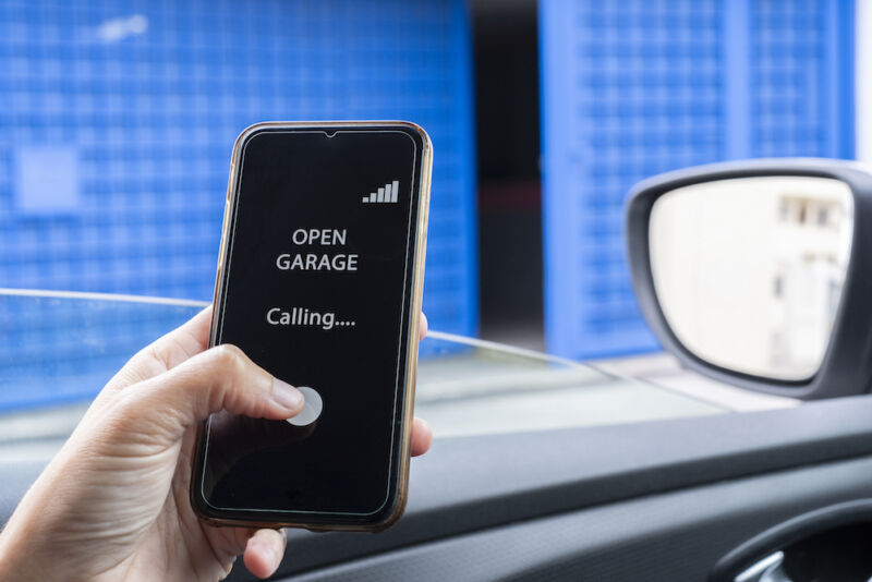 Woman inside car using mobile phone to open garage.  A woman inserts a pin into a smartphone while opening a garage.