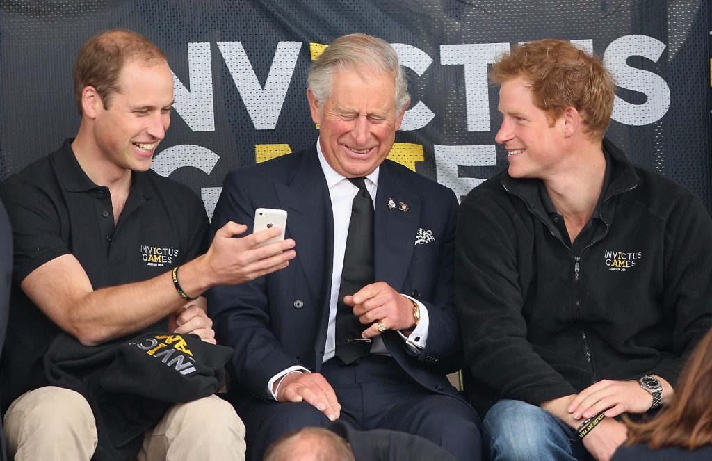 LONDON, ENGLAND - SEPTEMBER 11: Prince William, Duke of Cambridge, Prince Harry and Prince Charles, Prince of Wales look at a mobile phone as they watch Lee Valley Track athletics during the Invictus Games on September 11, 2014 in London, England.  The international sporting event of 